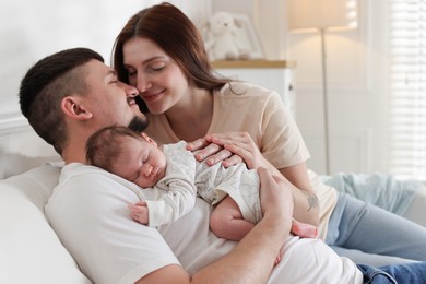 Photo of Happy parents with their cute newborn baby on sofa indoors