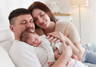 Photo of Happy parents with their cute newborn baby on sofa indoors