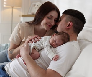 Photo of Happy parents with their cute newborn baby on sofa indoors