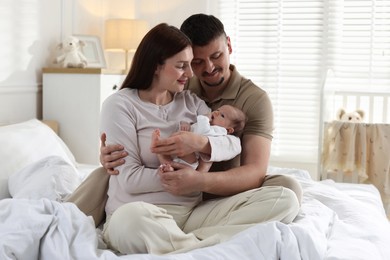 Photo of Happy parents with their cute newborn baby on bed indoors