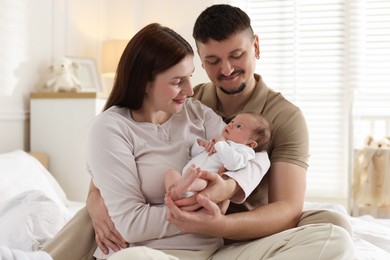Photo of Happy parents with their cute newborn baby on bed indoors