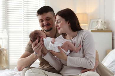 Photo of Happy parents with their cute newborn baby on bed indoors