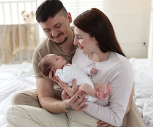 Photo of Happy parents with their cute newborn baby on bed indoors