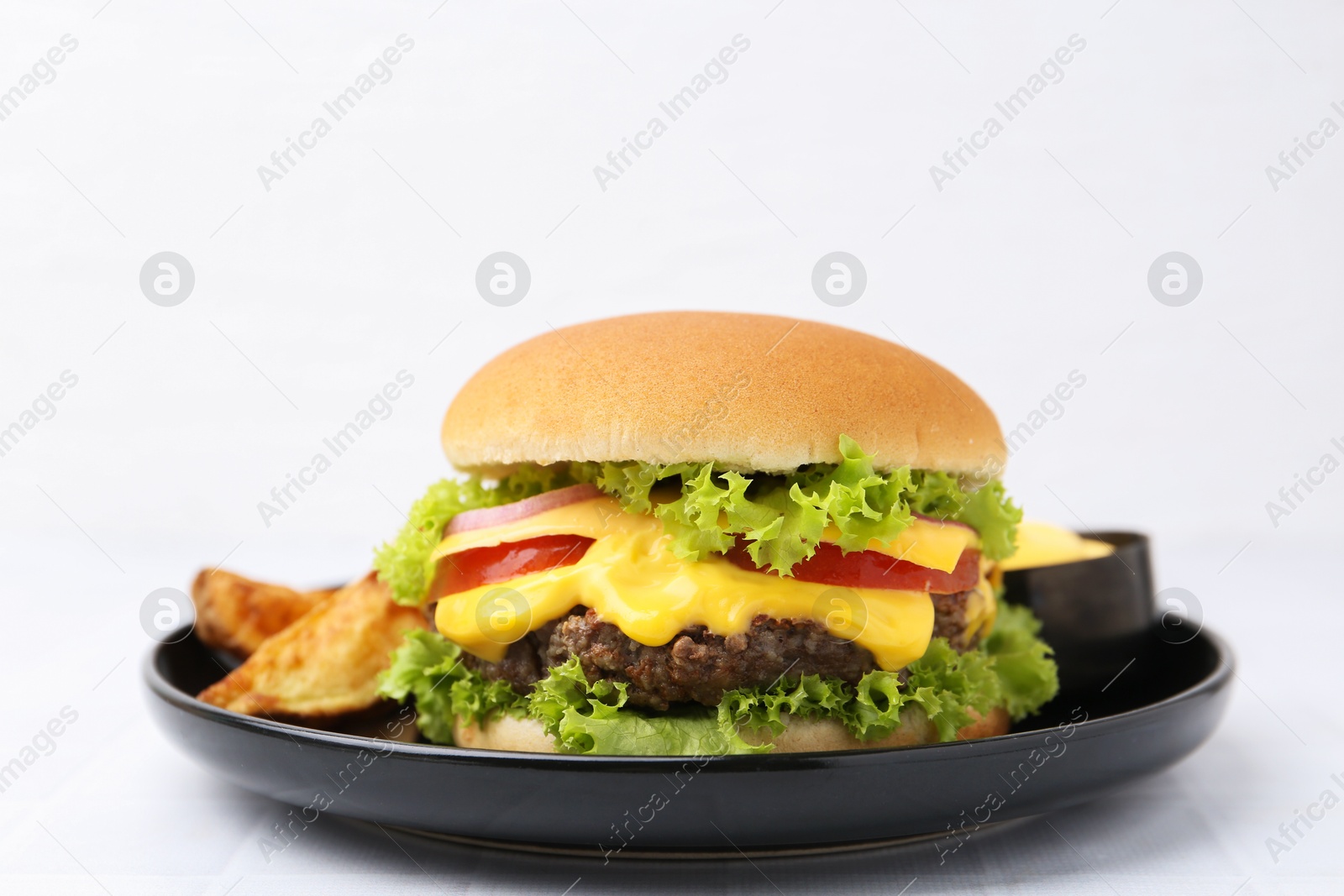 Tasty cheeseburger with sauce and potato wedges on white table, closeup Photo of Tasty cheeseburger with sauce and potato wedges on white table, closeup