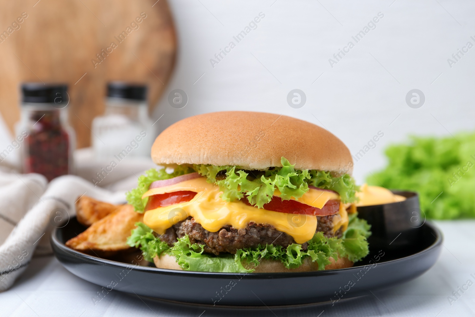 Tasty cheeseburger with sauce and potato wedges on white table, closeup Photo of Tasty cheeseburger with sauce and potato wedges on white table, closeup