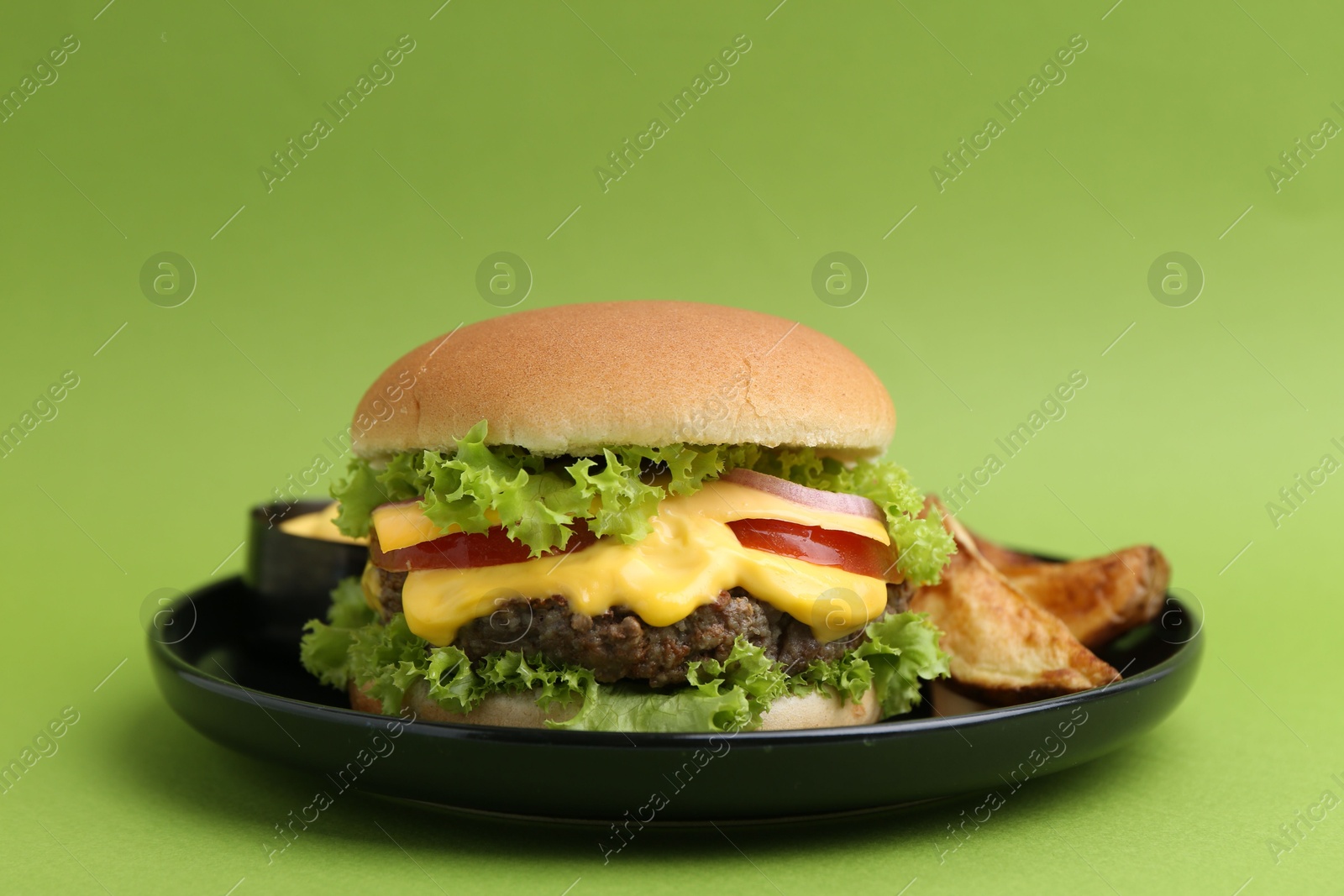 Tasty cheeseburger with sauce and potato wedges on green background, closeup Photo of Tasty cheeseburger with sauce and potato wedges on green background, closeup