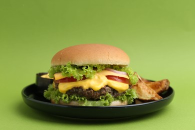 Photo of Tasty cheeseburger with sauce and potato wedges on green background, closeup