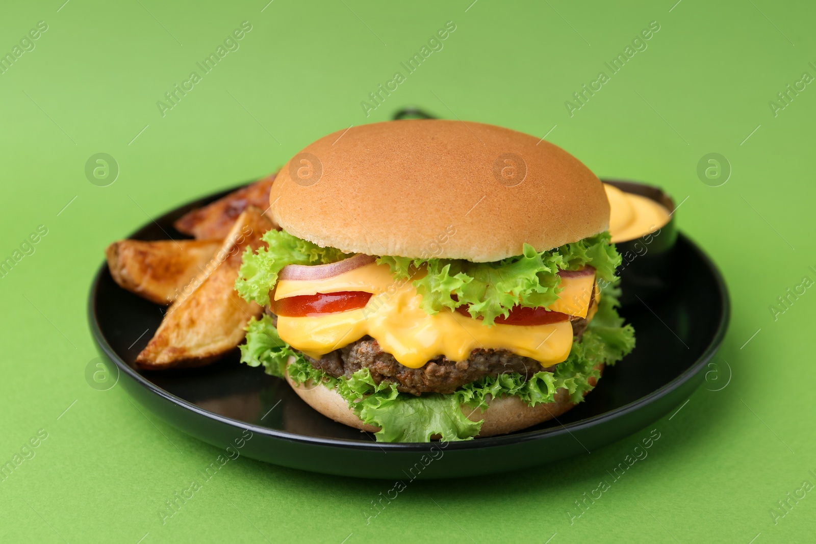 Tasty cheeseburger with sauce and potato wedges on green background, closeup Photo of Tasty cheeseburger with sauce and potato wedges on green background, closeup
