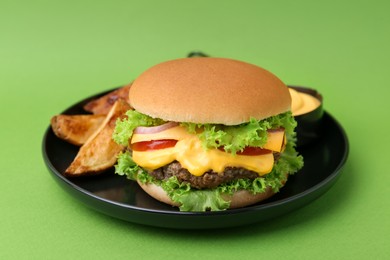 Photo of Tasty cheeseburger with sauce and potato wedges on green background, closeup