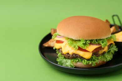 Photo of Tasty cheeseburger with sauce and potato wedges on green background, closeup. Space for text