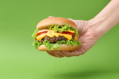 Photo of Woman with tasty cheeseburger on green background, closeup