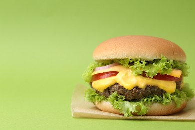 Photo of Tasty cheeseburger with sauce on green background, closeup. Space for text