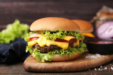 Photo of Tasty cheeseburger with sauce on wooden table, closeup