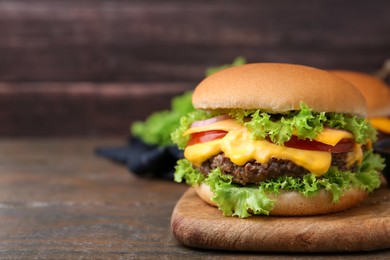 Photo of Tasty cheeseburger with sauce on wooden table, closeup. Space for text
