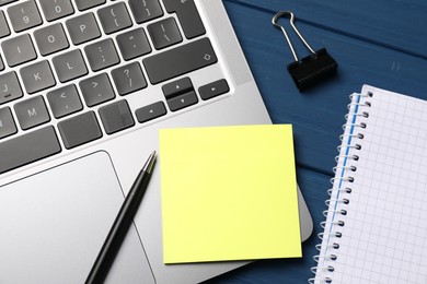 Photo of Laptop with sticky note, pen, paper clip and notebook on blue wooden table, closeup