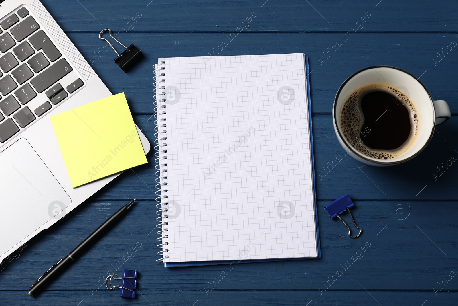 Notebook with pen, laptop, sticky note, paper clips and coffee on blue wooden table, flat lay Photo of Notebook with pen, laptop, sticky note, paper clips and coffee on blue wooden table, flat lay