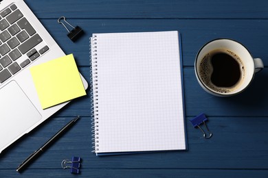 Photo of Notebook with pen, laptop, sticky note, paper clips and coffee on blue wooden table, flat lay