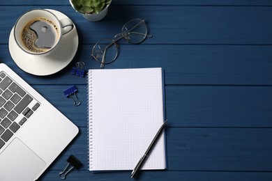 Photo of Notebook with pen, laptop, glasses, paper clips and coffee on blue wooden table, flat lay. Space for text