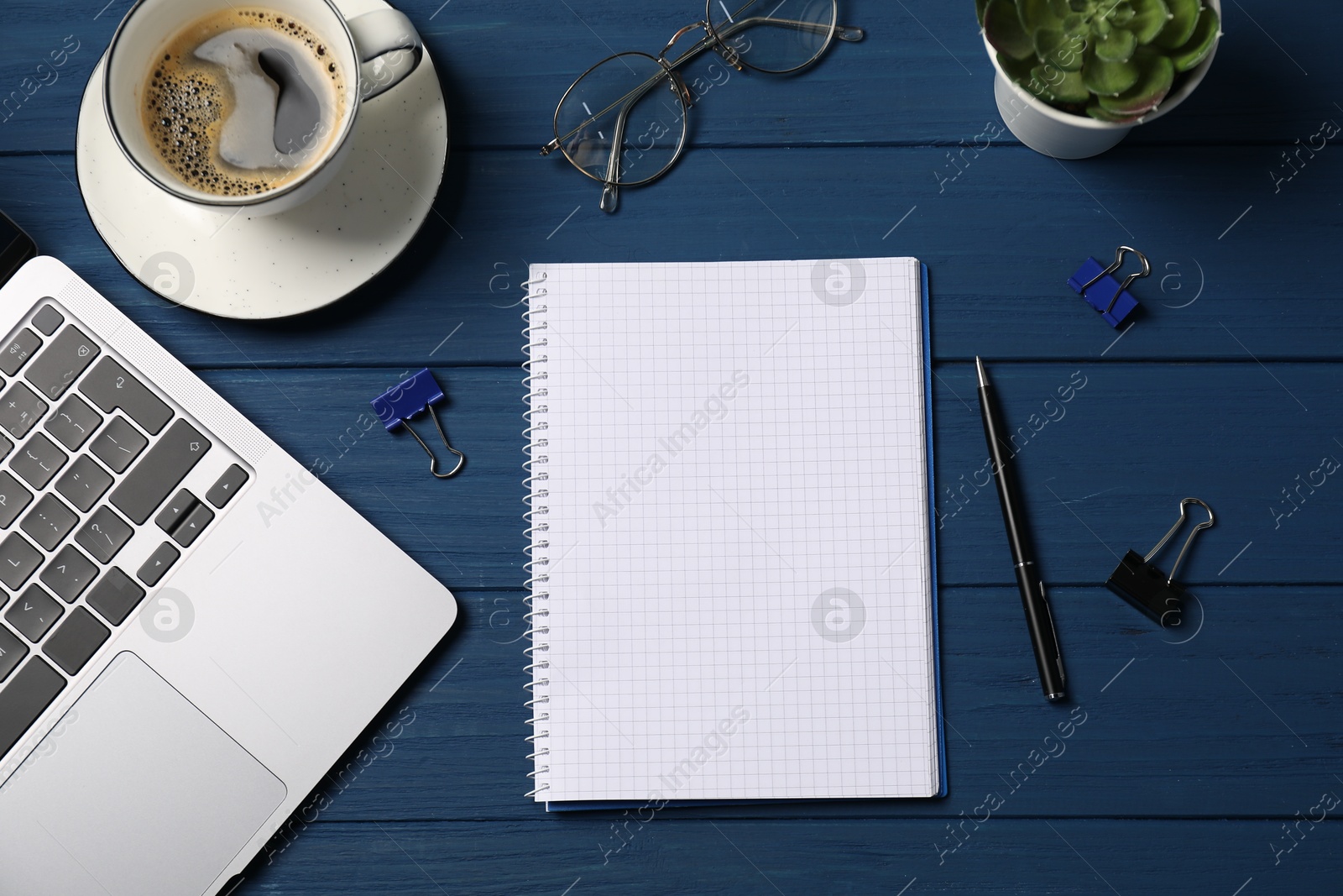 Photo of Notebook with pen, laptop, paper clips and coffee on blue wooden table, flat lay