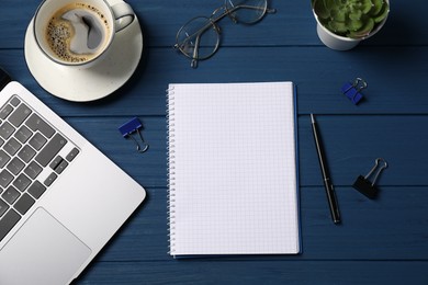 Photo of Notebook with pen, laptop, paper clips and coffee on blue wooden table, flat lay
