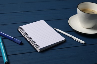 Photo of Notebook with pen, markers and coffee on blue wooden table, closeup