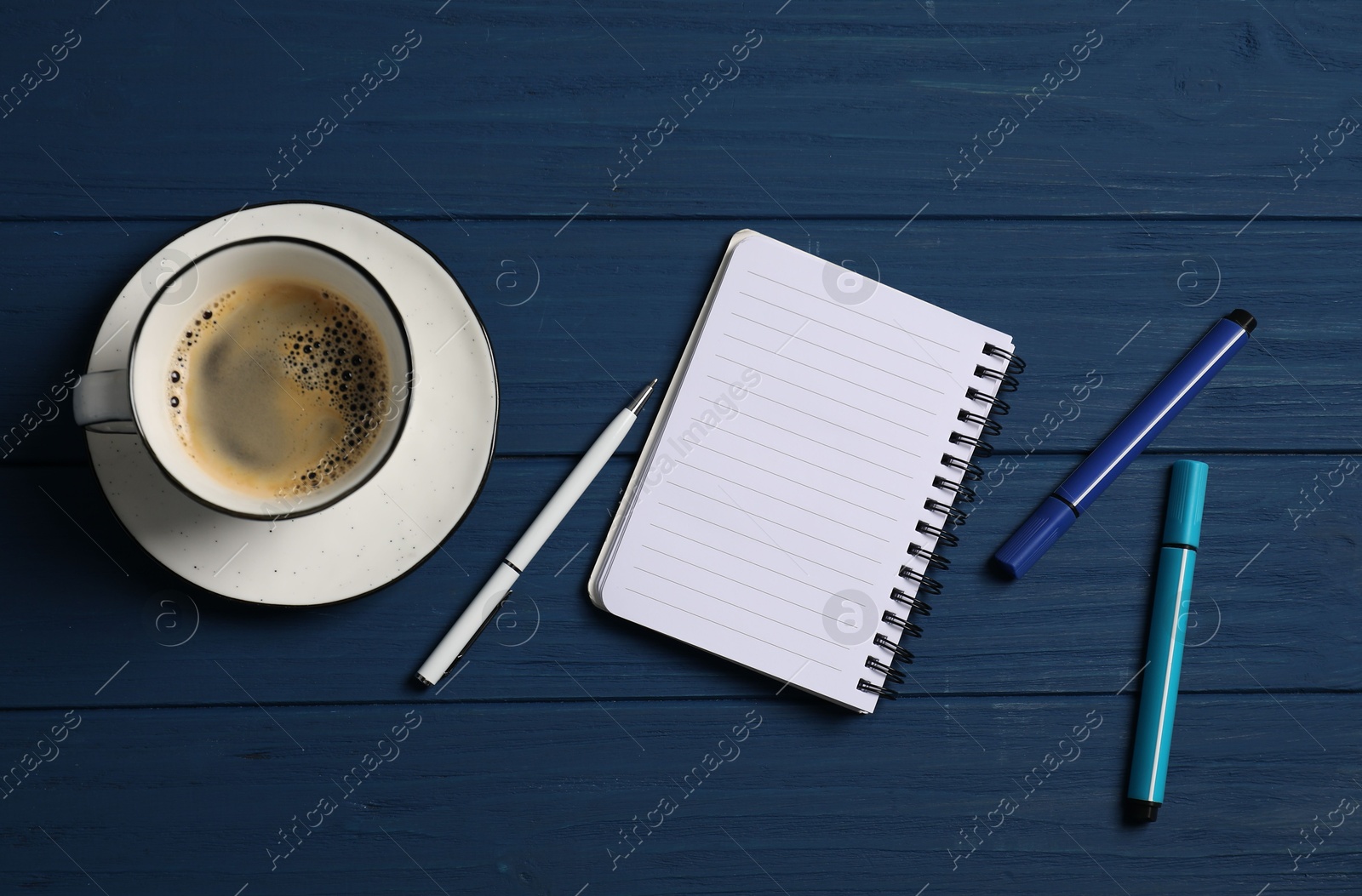 Photo of Notebook with pen, markers and coffee on blue wooden table, flat lay