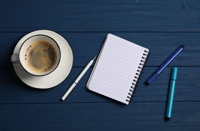 Photo of Notebook with pen, markers and coffee on blue wooden table, flat lay