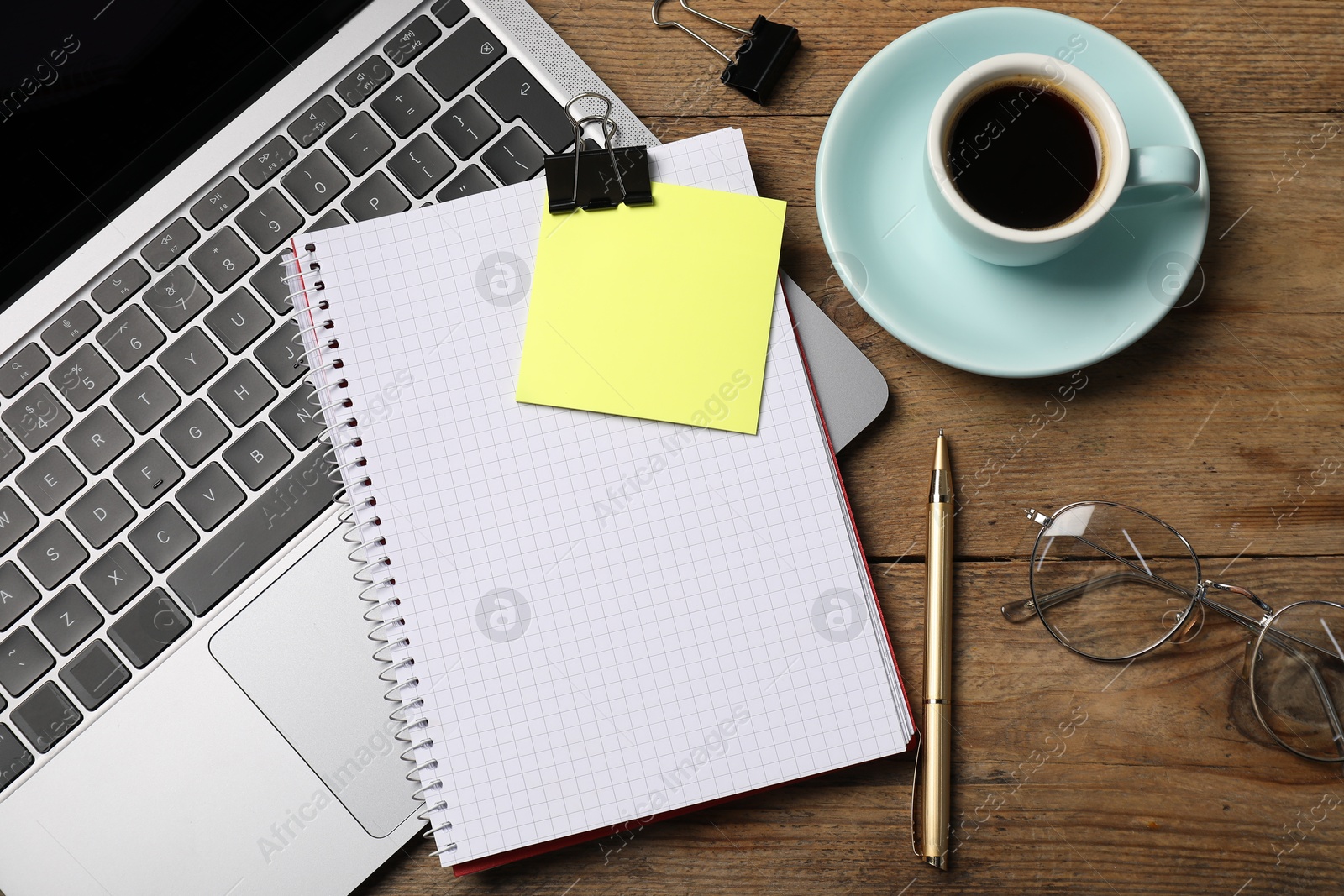 Notebook with pen, sticky note, laptop, paper clips and coffee on wooden table, flat lay Photo of Notebook with pen, sticky note, laptop, paper clips and coffee on wooden table, flat lay