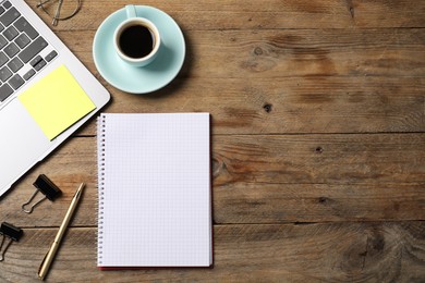 Photo of Notebook with pen, sticky note, laptop, paper clips and coffee on wooden table, flat lay. Space for text