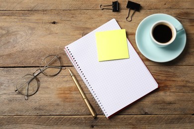 Photo of Notebook with pen, sticky note, glasses, paper clips and coffee on wooden table, flat lay
