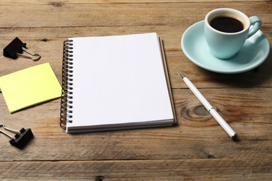 Photo of Notebook with pen, sticky note, paper clips and coffee on wooden table