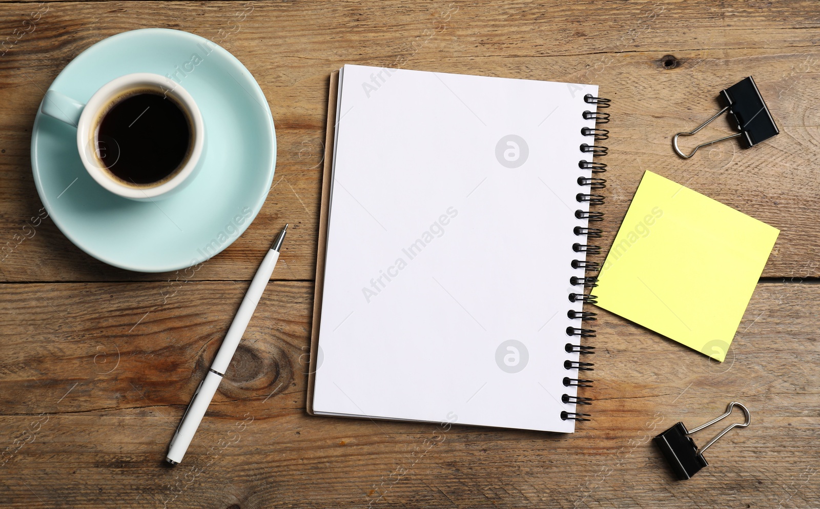 Notebook with pen, sticky note, paper clips and coffee on wooden table, flat lay Photo of Notebook with pen, sticky note, paper clips and coffee on wooden table, flat lay