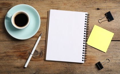 Photo of Notebook with pen, sticky note, paper clips and coffee on wooden table, flat lay