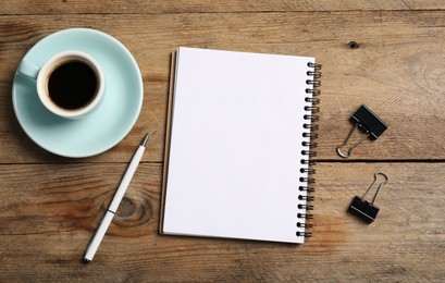 Photo of Notebook with pen, paper clips and coffee on wooden table, flat lay