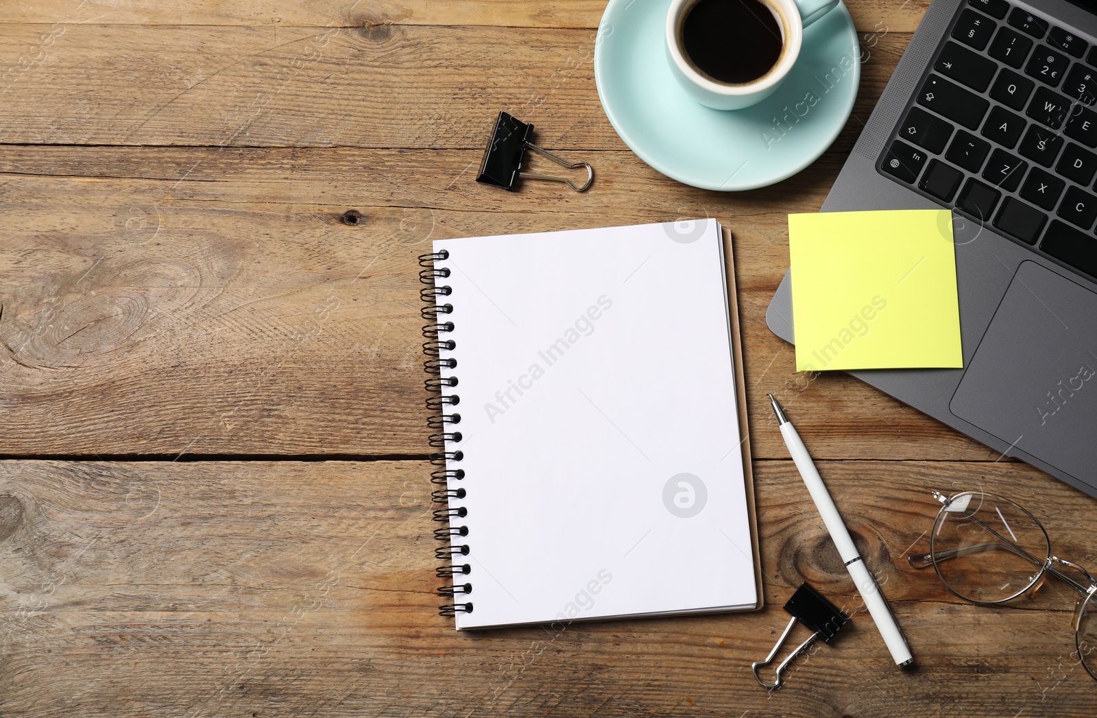 Photo of Notebook with pen, sticky note, laptop, paper clips and coffee on wooden table, flat lay. Space for text