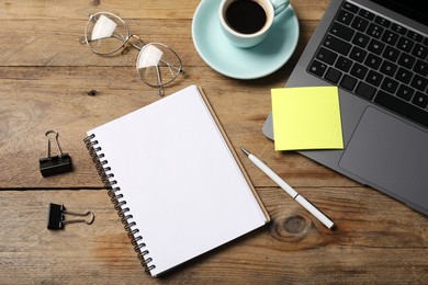 Photo of Notebook with pen, sticky note, laptop, paper clips and coffee on wooden table, flat lay