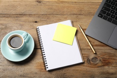 Photo of Notebook with pen, sticky note, laptop and coffee on wooden table, above view