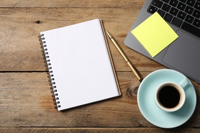 Photo of Notebook with pen, sticky note, laptop and coffee on wooden table, flat lay