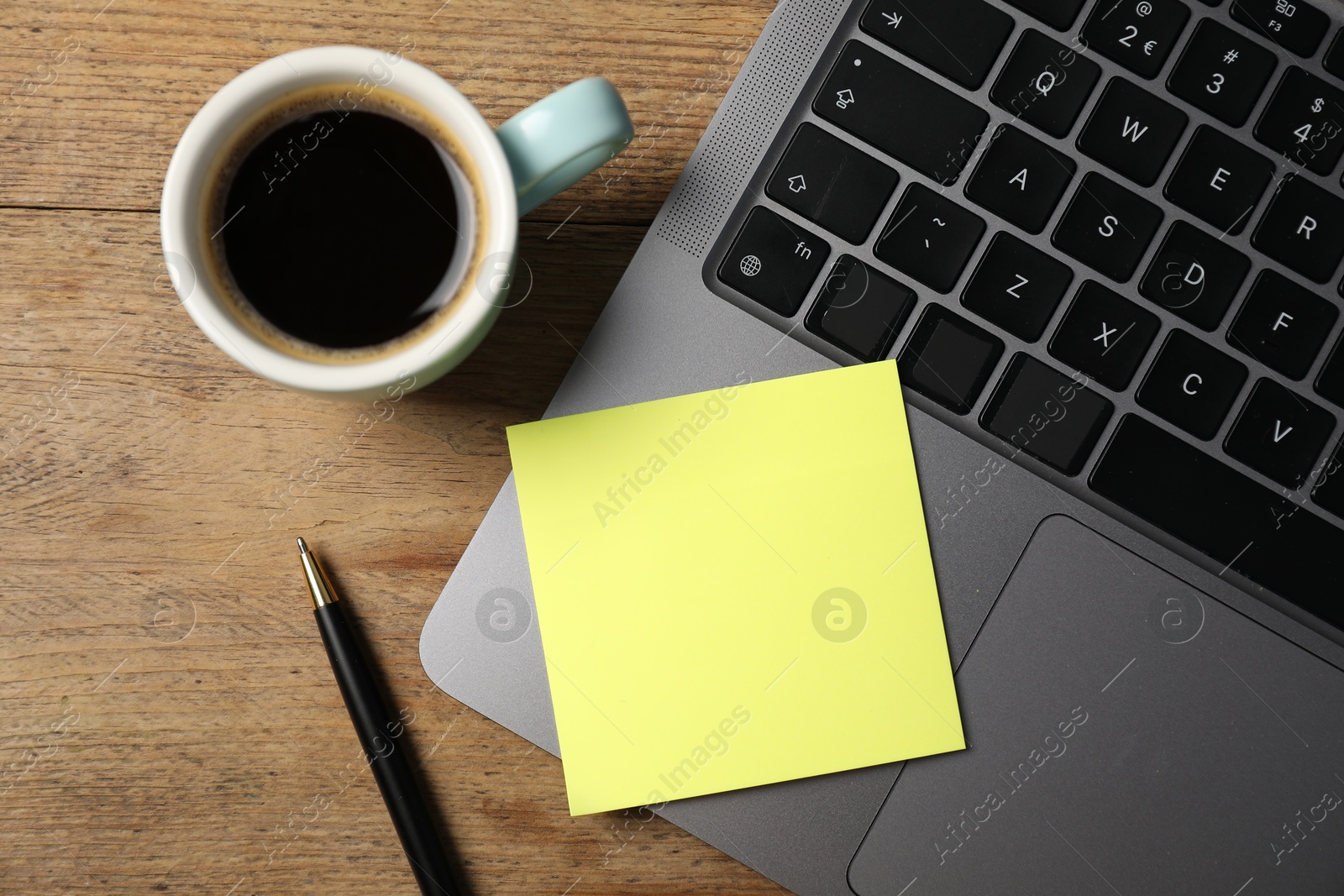Photo of Laptop with sticky note, pen and coffee on wooden table, top view