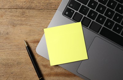 Photo of Laptop with sticky note and pen on wooden table, top view