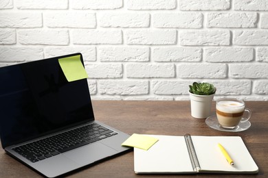 Photo of Laptop with sticky note, notebook, pen, coffee and plant on wooden table. Space for text
