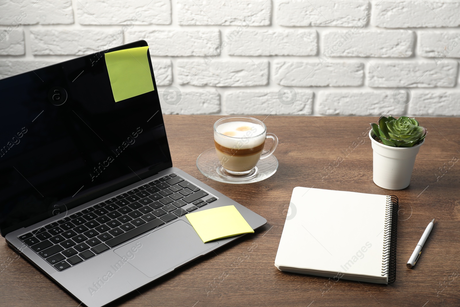 Laptop with sticky note, notebook, pen, coffee and plant on wooden table Photo of Laptop with sticky note, notebook, pen, coffee and plant on wooden table