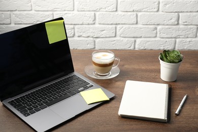 Photo of Laptop with sticky note, notebook, pen, coffee and plant on wooden table