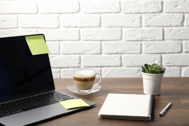 Photo of Laptop with sticky note, notebook, pen, coffee and plant on wooden table. Space for text