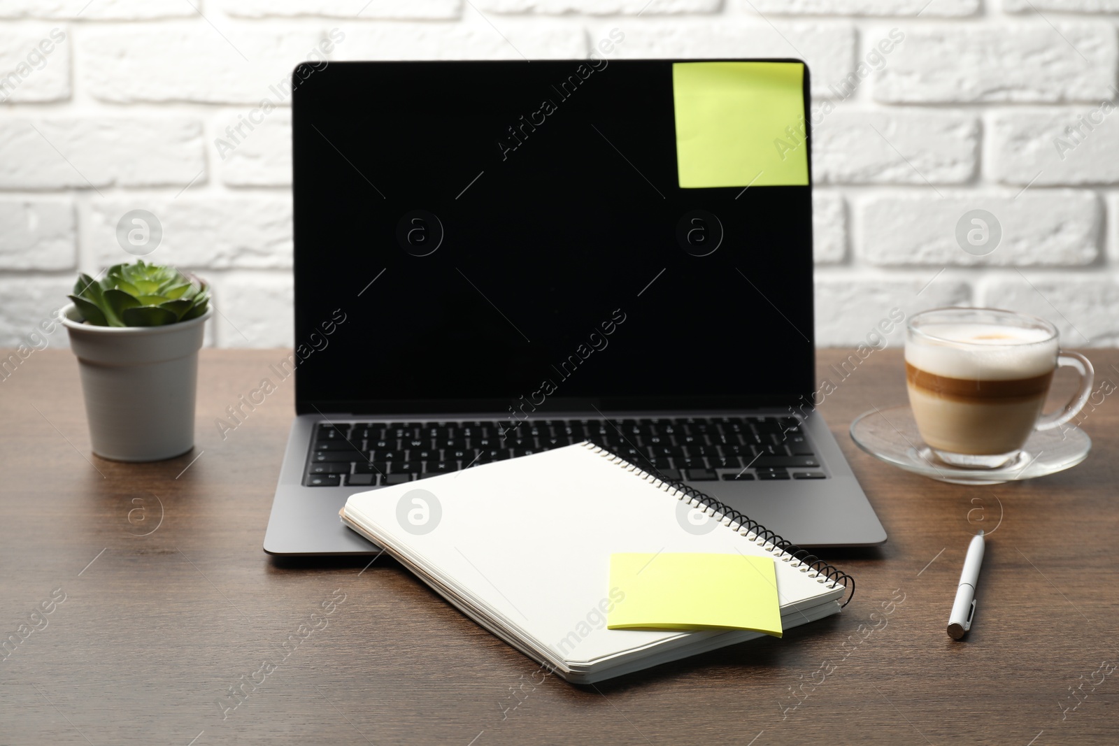 Laptop with sticky note, notebook, pen, coffee and plant on wooden table Photo of Laptop with sticky note, notebook, pen, coffee and plant on wooden table