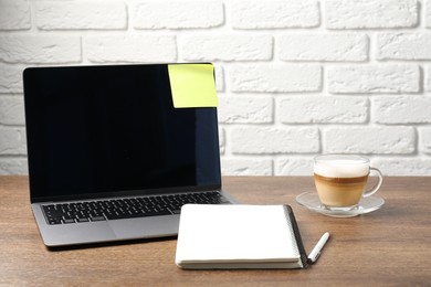 Photo of Laptop with sticky note, notebook, coffee and pen on wooden table. Space for text