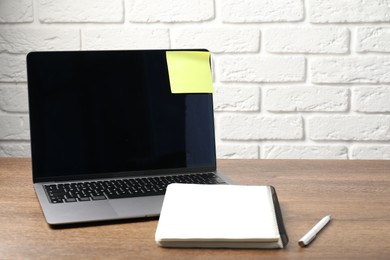 Photo of Laptop with sticky note, notebook and pen on wooden table. Space for text