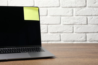 Photo of Laptop with sticky note on wooden table. Space for text