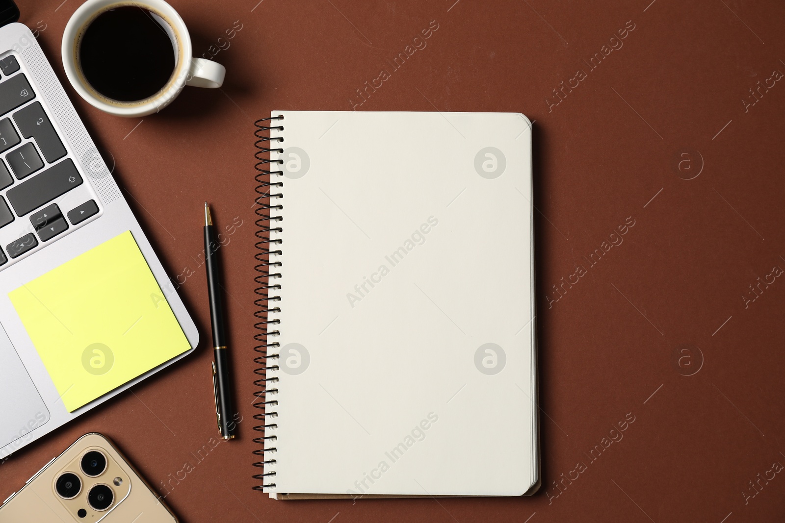 Photo of Notebook with pen, laptop, smartphone, sticky note and coffee on brown background, flat lay
