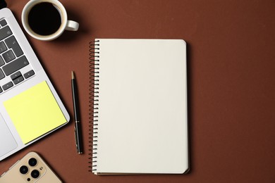 Photo of Notebook with pen, laptop, smartphone, sticky note and coffee on brown background, flat lay